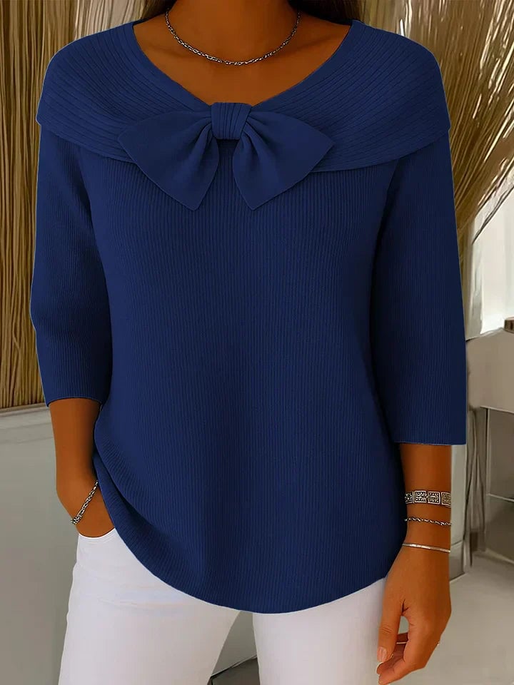 Dark blue knit bow sweater draped over a chair, showing full-length relaxed fit and color detail