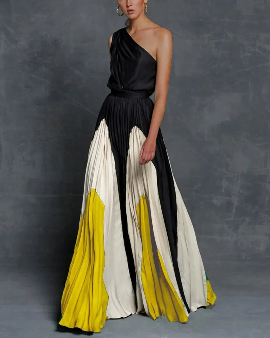 Woman wearing the Vivienne one-shoulder color block pleated maxi dress in yellow, showing the full floor-length silhouette