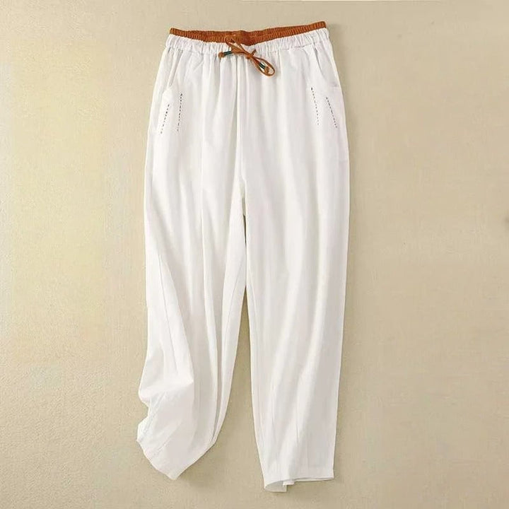 Woman wearing white relaxed-fit summer pants with a contrast cinnamon waistband, standing in a bright outdoor setting