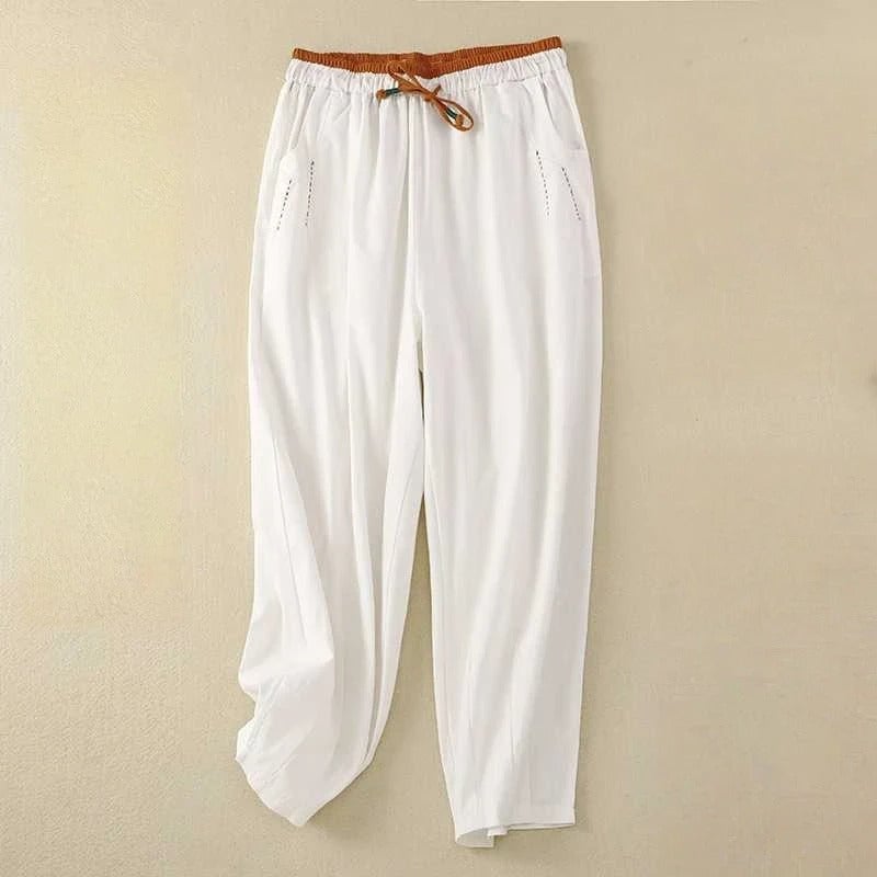 Woman wearing white relaxed-fit summer pants with a contrast cinnamon waistband, standing in a bright outdoor setting