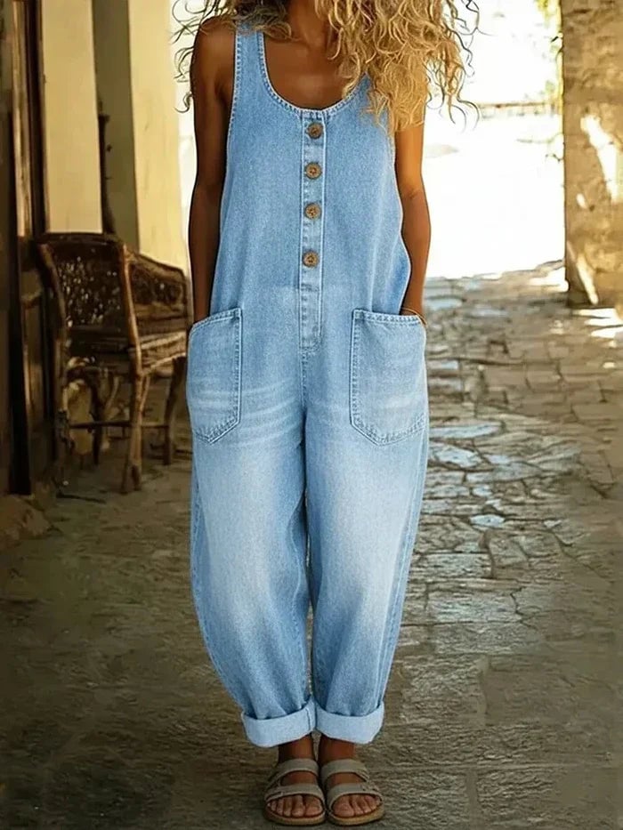 Woman wearing loose fit sleeveless denim overalls in light blue with wooden-style button front detail and rolled cuffs