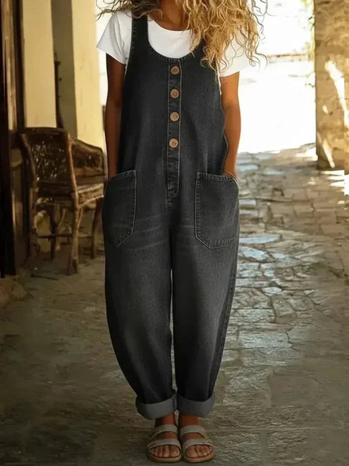 Side profile of women's loose fit denim overalls in blue with wide shoulder straps and rolled hem